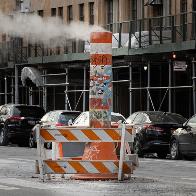 A gritty New York street scene with steam rising from a graffiti-covered vent.